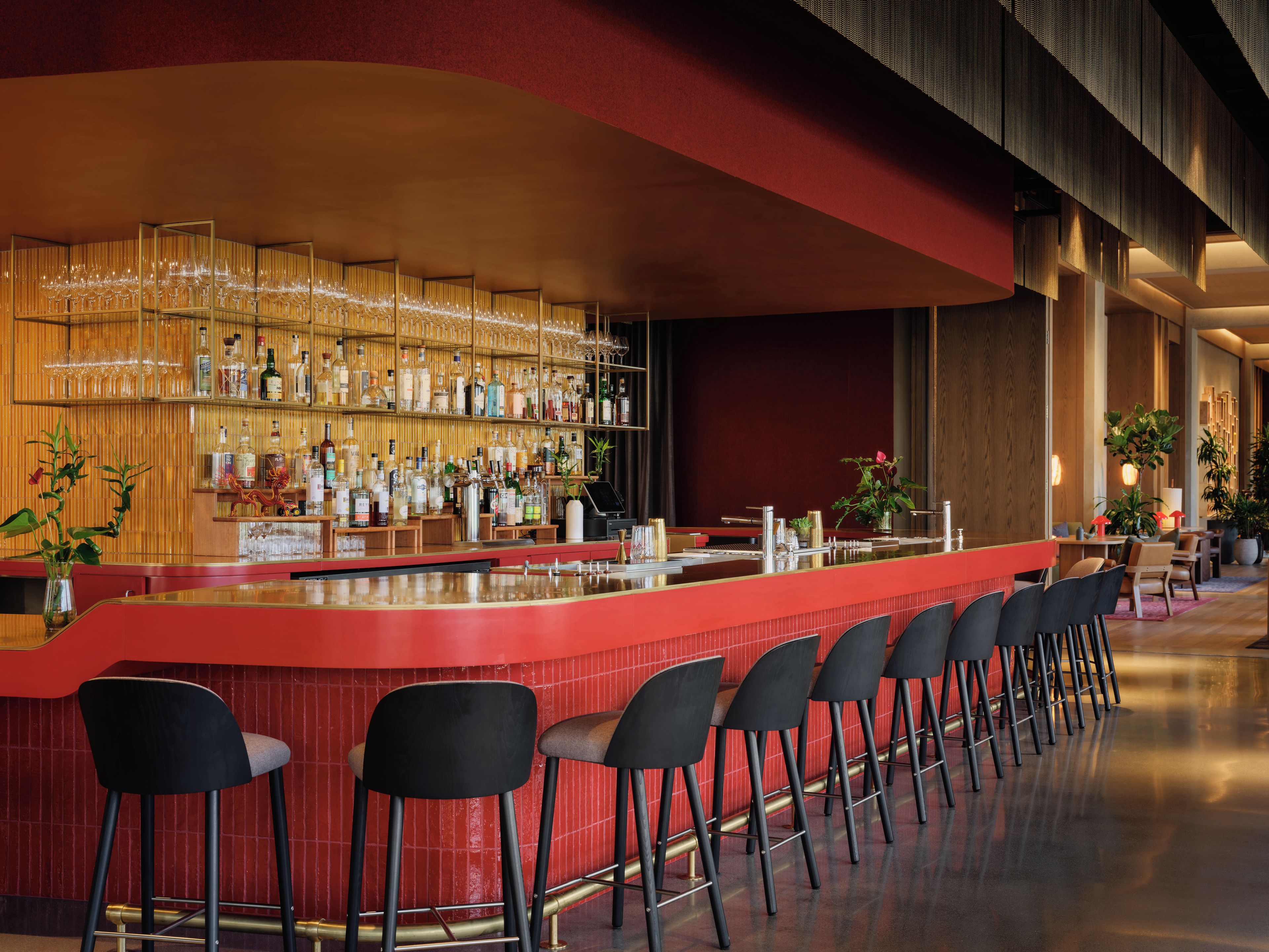 A bar area with a long counter, multiple stools, and a variety of bottles and glasses.