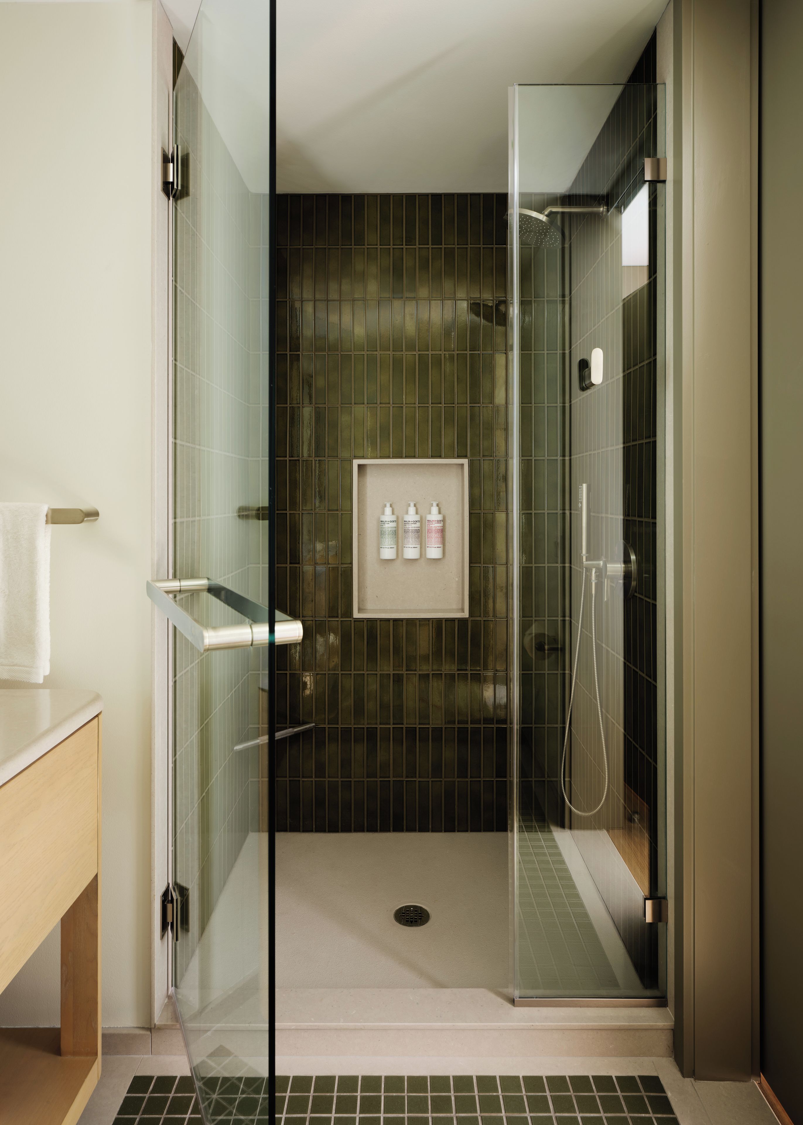 A modern bathroom with a glass shower enclosure, a framed set of toiletries, and a towel rack.