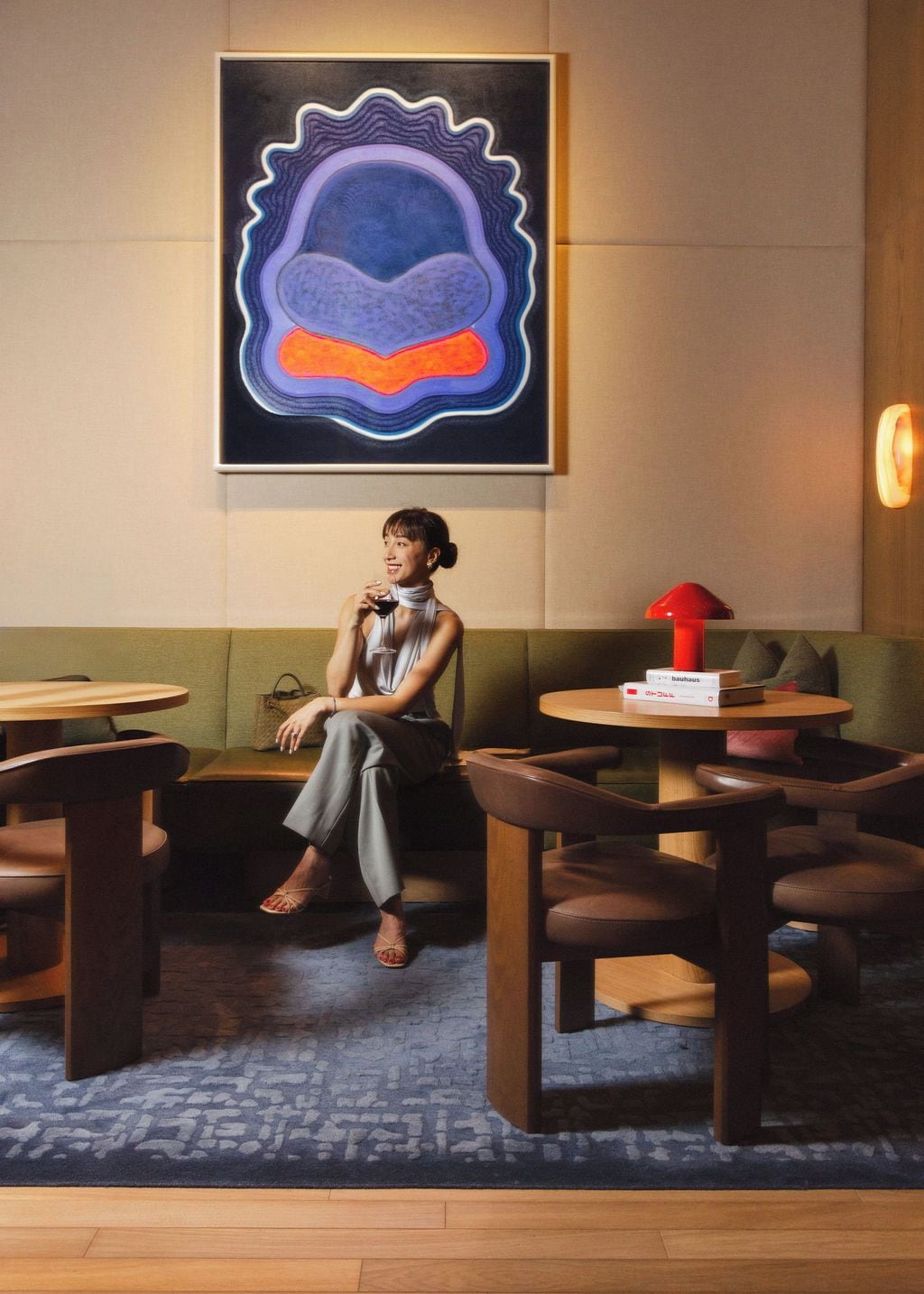 A woman seated on a sofa in a room with a round table, a red lamp, and a Bauhaus-branded box.