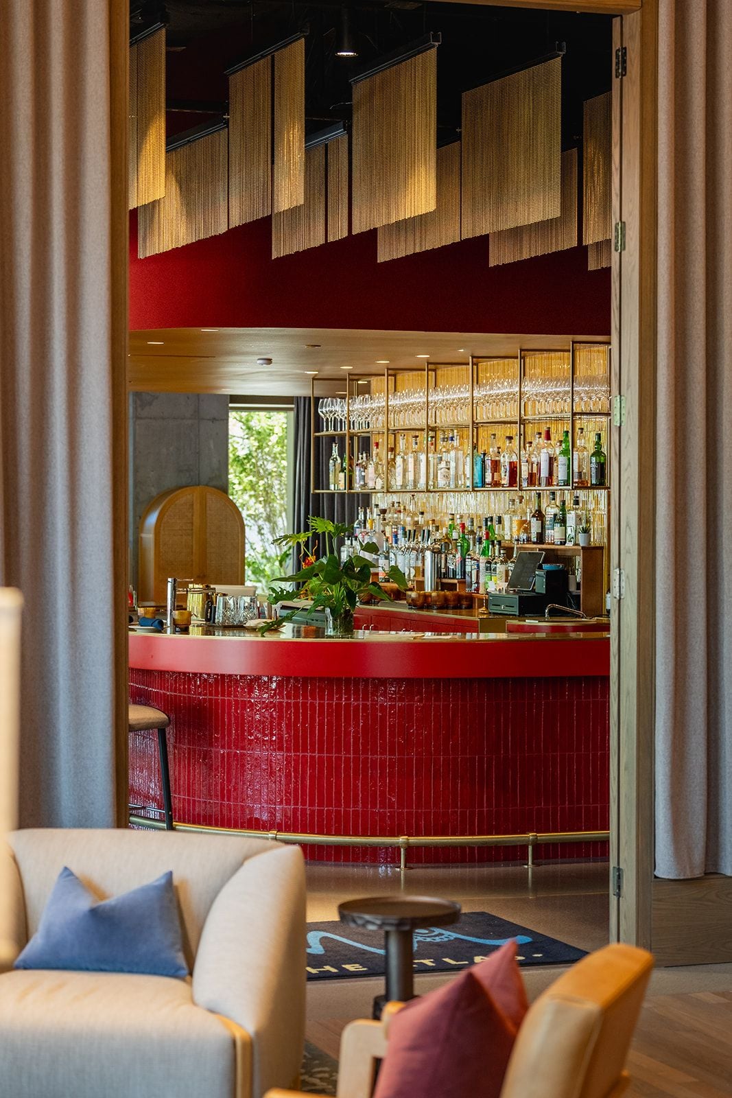 A bar area with a red counter, shelves of bottles, and a seating area with chairs and a round table.