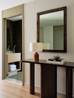 A modern bathroom with a wooden console table, a mirror, a towel rack, and a small plant.