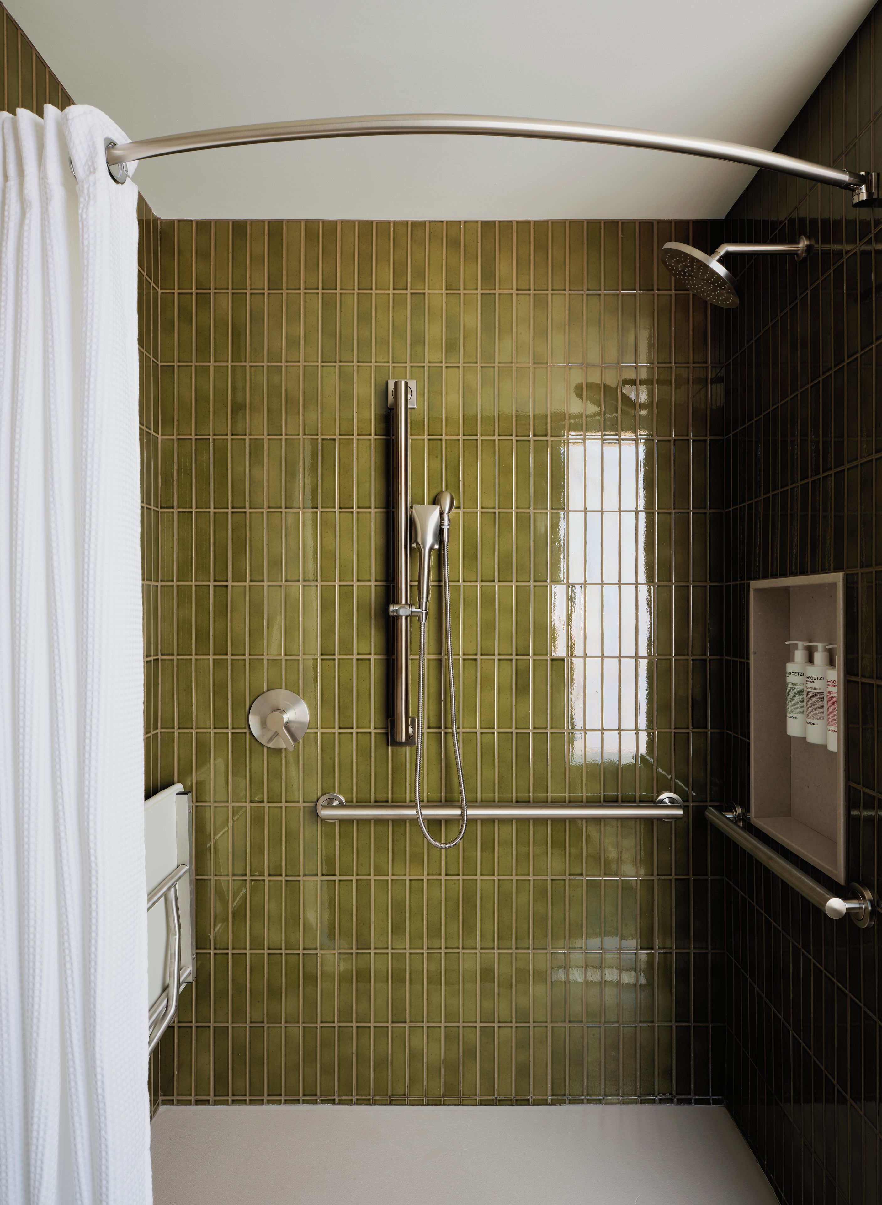 A shower area with a grab bar, a handheld showerhead, and a towel rack.