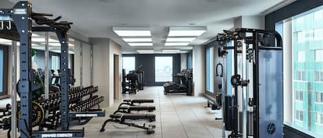 A modern gym with various exercise equipment, large windows, and a clean, spacious layout.