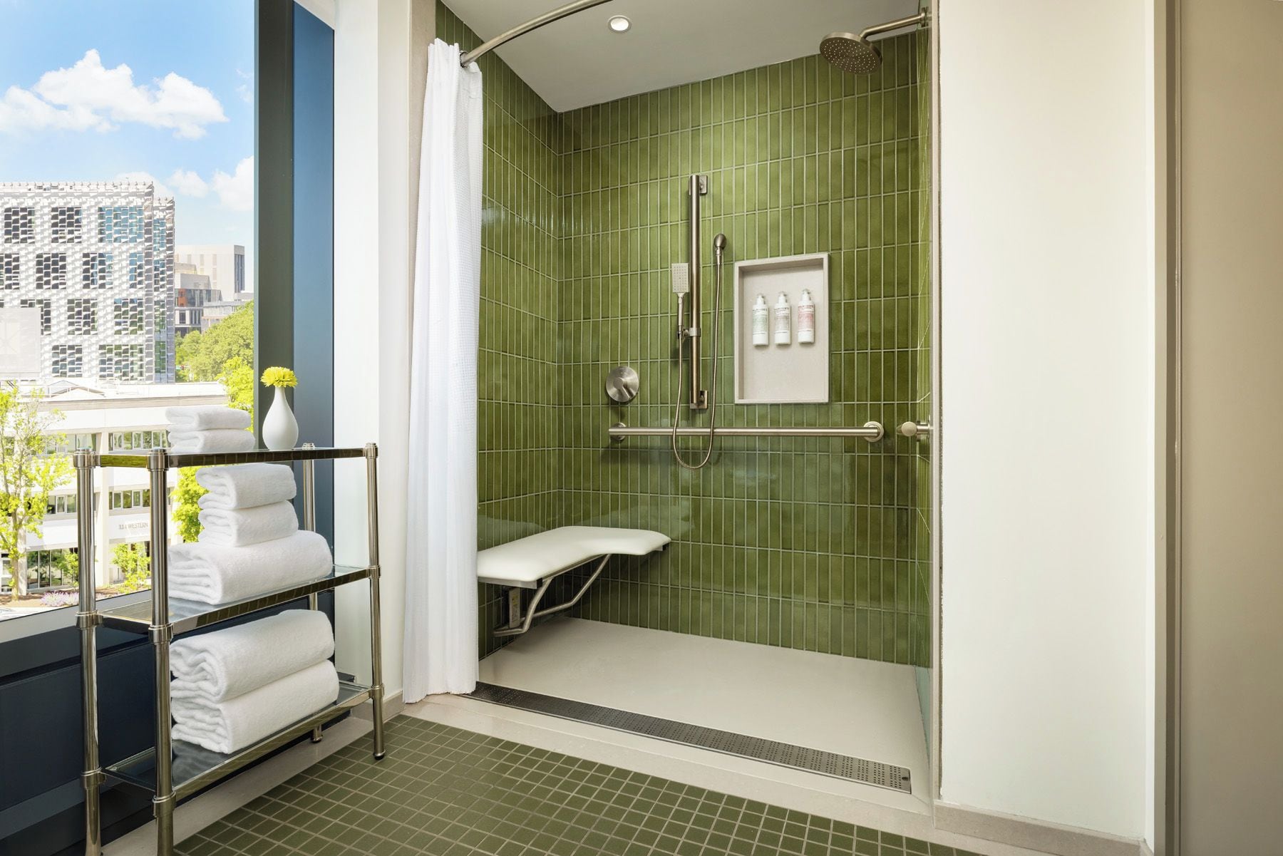 A modern bathroom with a glass shower enclosure, a white bench, and a towel rack with folded towels.