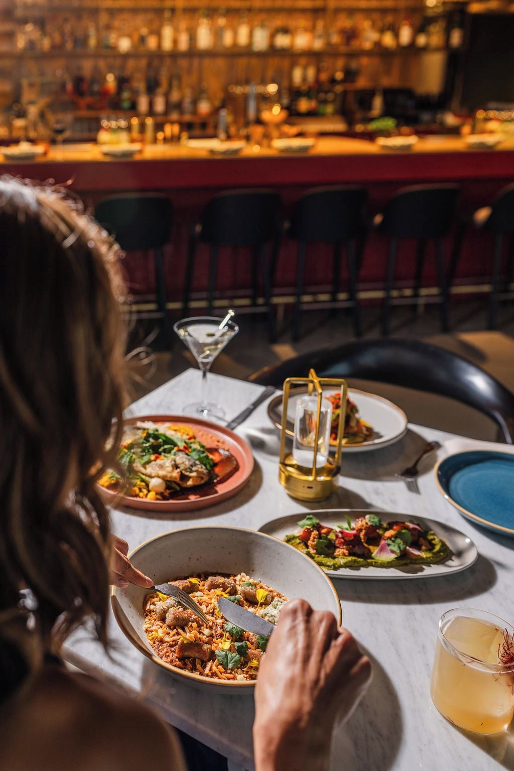 A dining table with plates of food, a martini glass, and a candle.