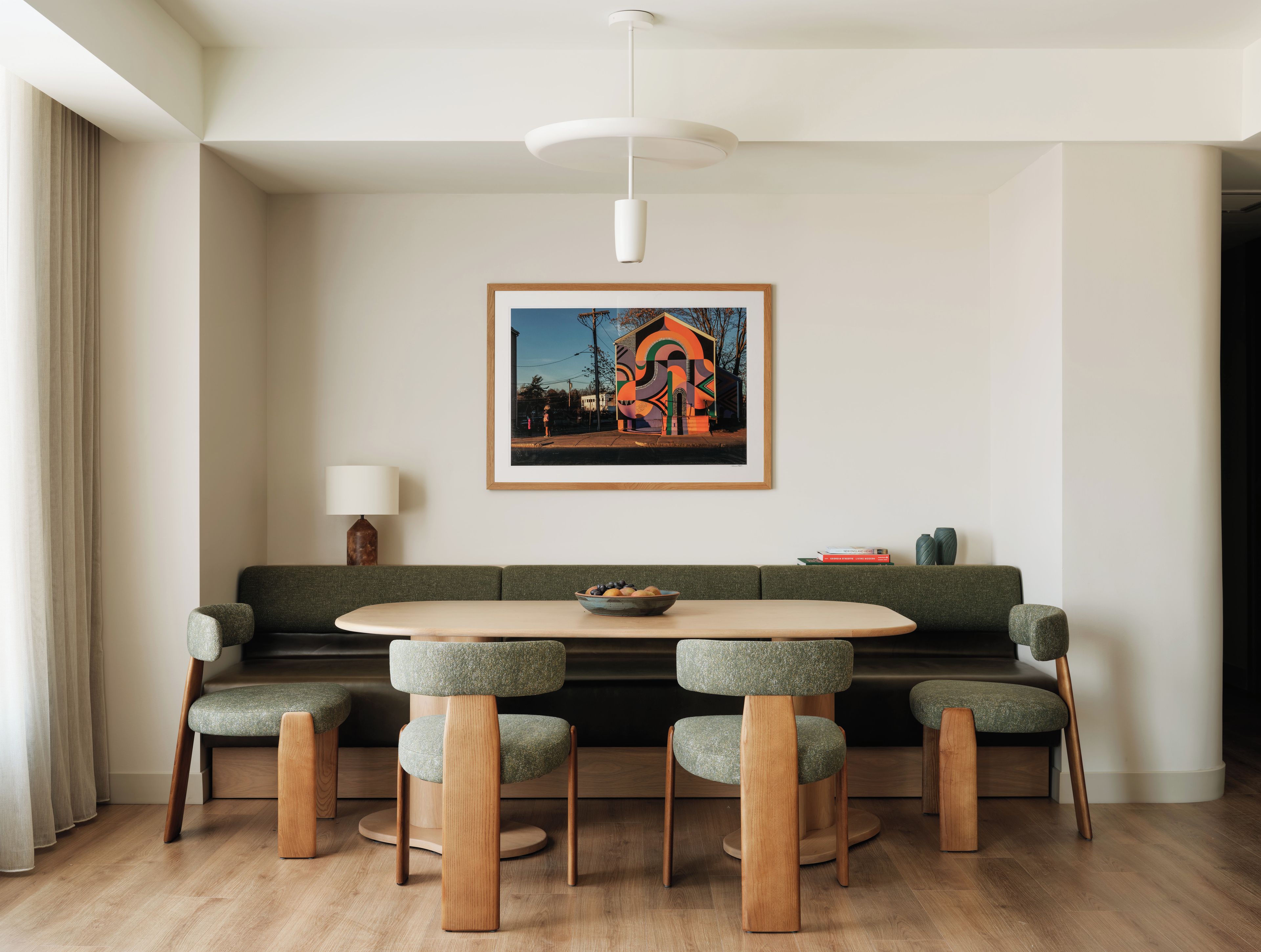 Un comedor moderno con una mesa redonda, seis sillas, un sofá verde y una obra de arte enmarcada en la pared.