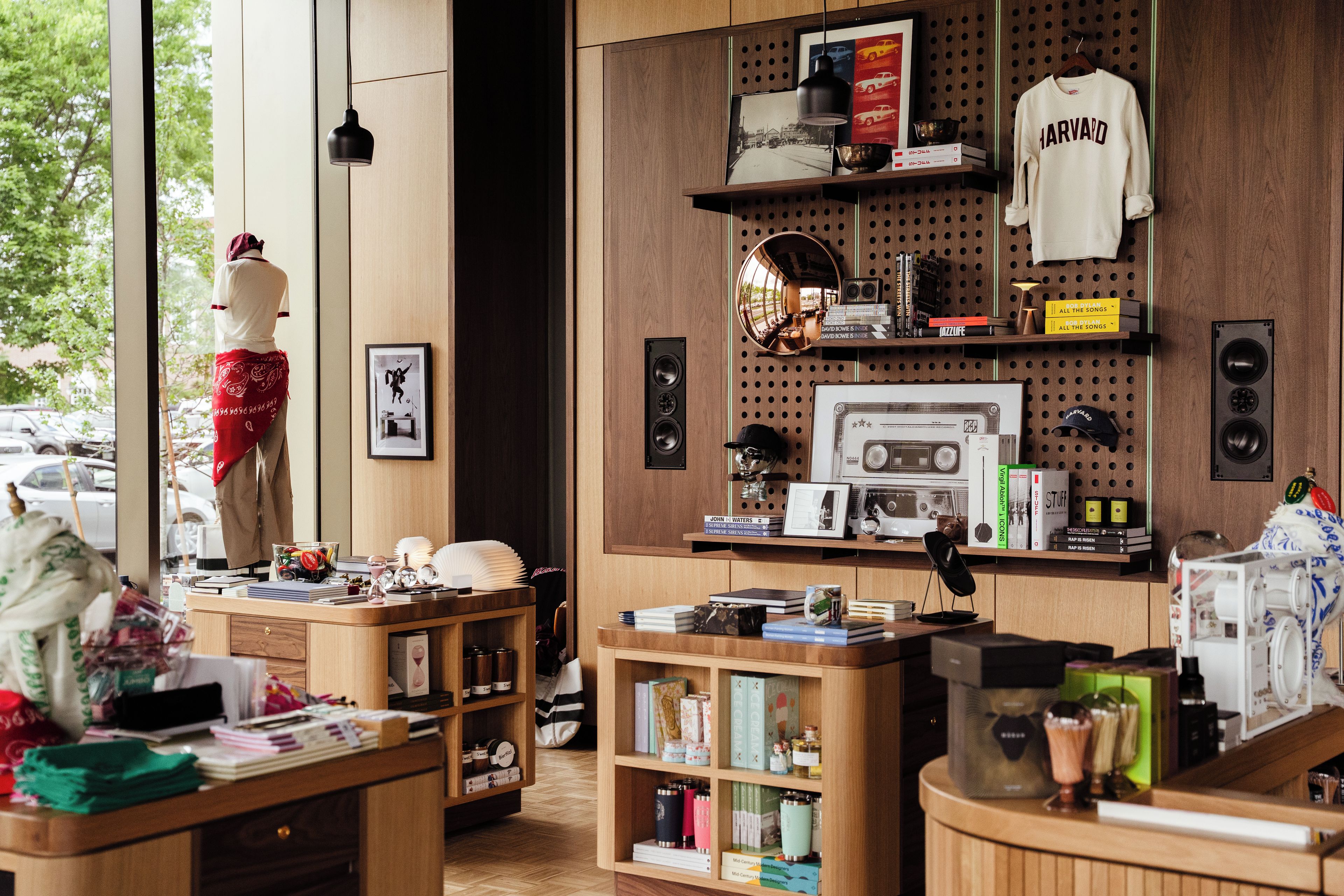 Una habitación con un maniquí, estanterías con libros y objetos decorativos, un espejo y una ventana con vistas al exterior.