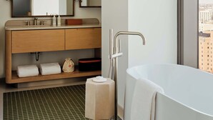 A modern bathroom with a large bathtub, a vanity with a mirror, and a view of the city through a large window. - The Atlas Hotel Boston Cambridge (Boston)