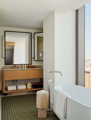 A modern bathroom with a large bathtub, a vanity with a mirror, and a view of the city through a large window.