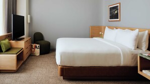 A hotel room with a bed, a TV, a desk, a chair, and a small table with a vase of flowers. - The Atlas Hotel Boston Cambridge (Boston)