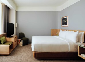 A hotel room with a bed, a TV, a desk, a chair, and a small table with a vase of flowers.