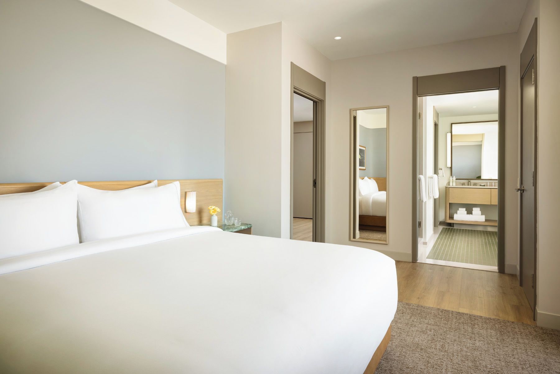 A hotel room with a large bed, a bedside table, a mirror, and a bathroom visible through an open door.