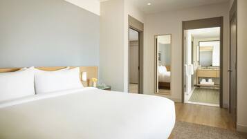 A hotel room with a large bed, a bedside table, a mirror, and a bathroom visible through an open door.