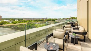 A rooftop terrace with outdoor seating, a glass balustrade, and a view of a building and greenery. - The Atlas Hotel Boston Cambridge (Boston)