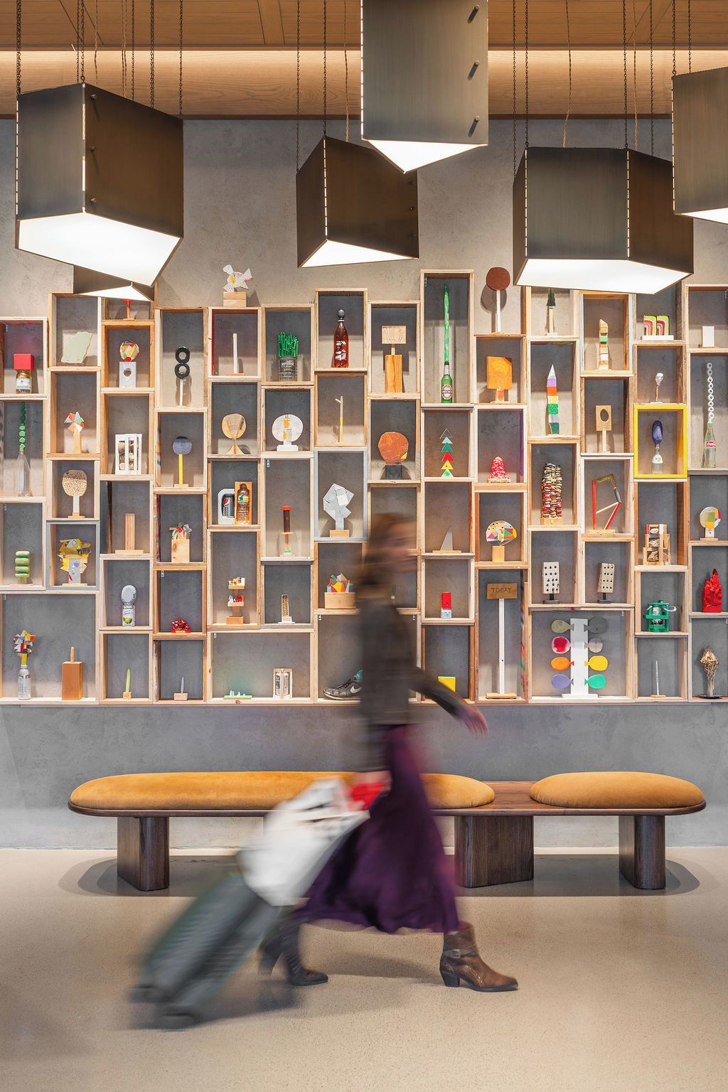 Un interior moderno con un banco central, estanterías de madera con diversos objetos y lámparas colgantes.