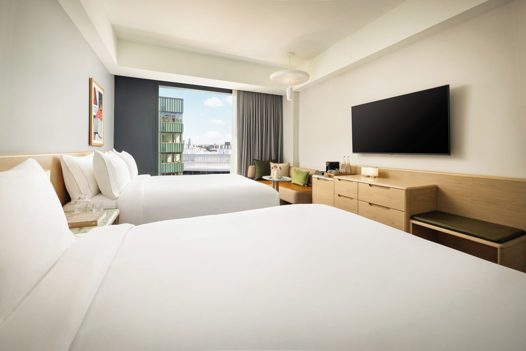Une chambre d’hôtel avec deux lits, un téléviseur à écran plat, un bureau avec une lampe et une vue sur la ville.