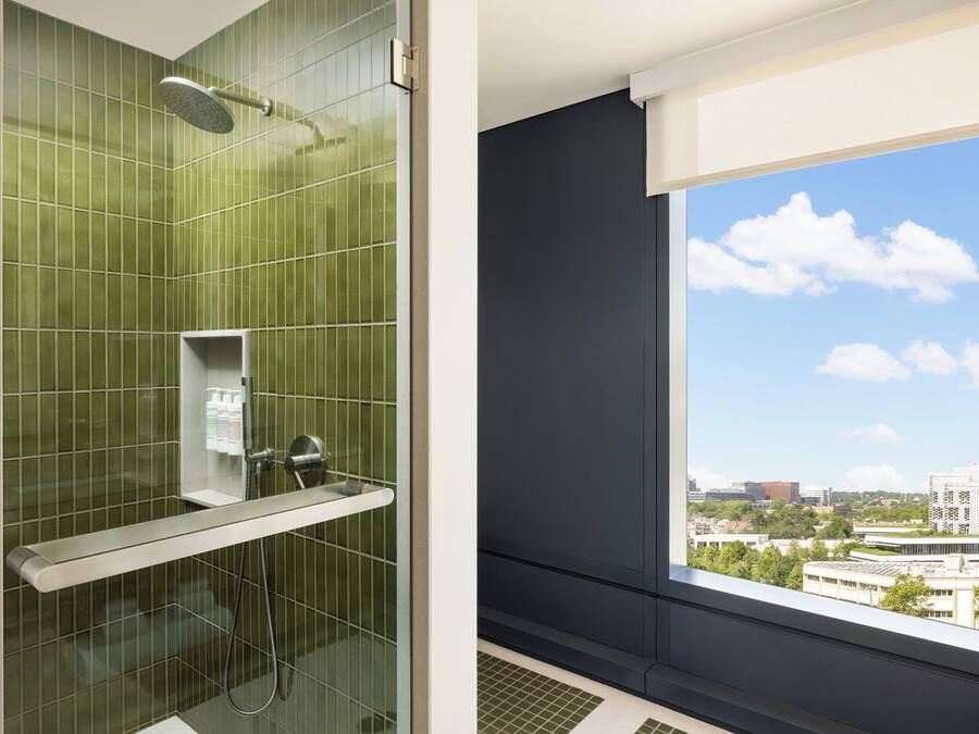 Ein modernes Badezimmer mit Duschkabine aus Glas, integriertem WC und einem Fenster mit Blick auf die Stadt.