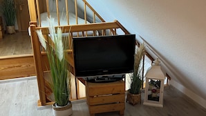 Een slaapkamer met een bed, een televisie op een houten dressoir, potplanten en een houten trap.