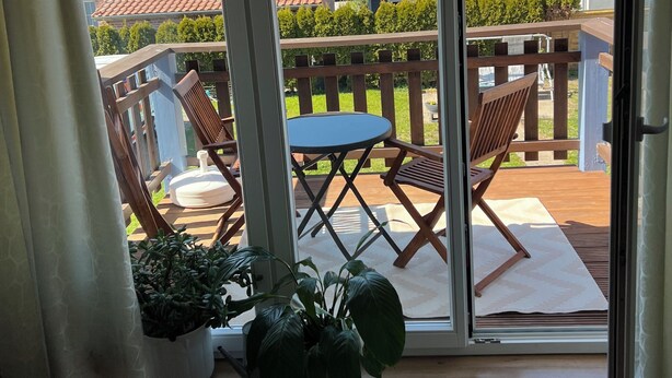 Een balkon met een tafel en stoelen, plantenbakken en uitzicht op omliggende huizen.