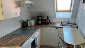 Een compacte keuken met een ingebouwde oven, een vaatwasser, een koffiezetapparaat en een raam boven de spoelbak.