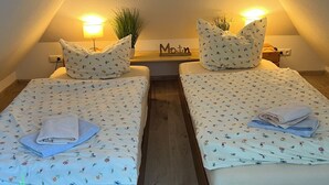 Twee eenpersoonsbedden met bloemenbeddengoed, nachtlampjes, een kleine potplant en een bordje met de tekst 'Main' aan de muur.