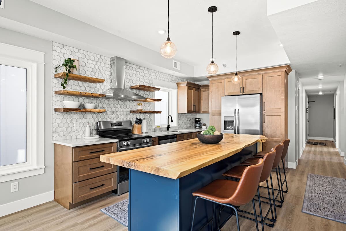 A modern kitchen with a central island, wooden cabinets, and pendant lighting.