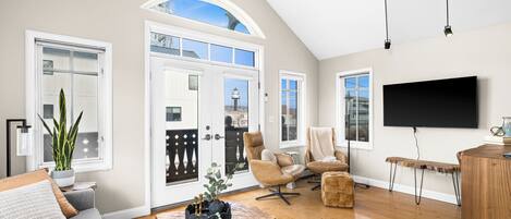 A spacious living room with a large TV, comfortable seating, a wooden coffee table, and a view through the door.