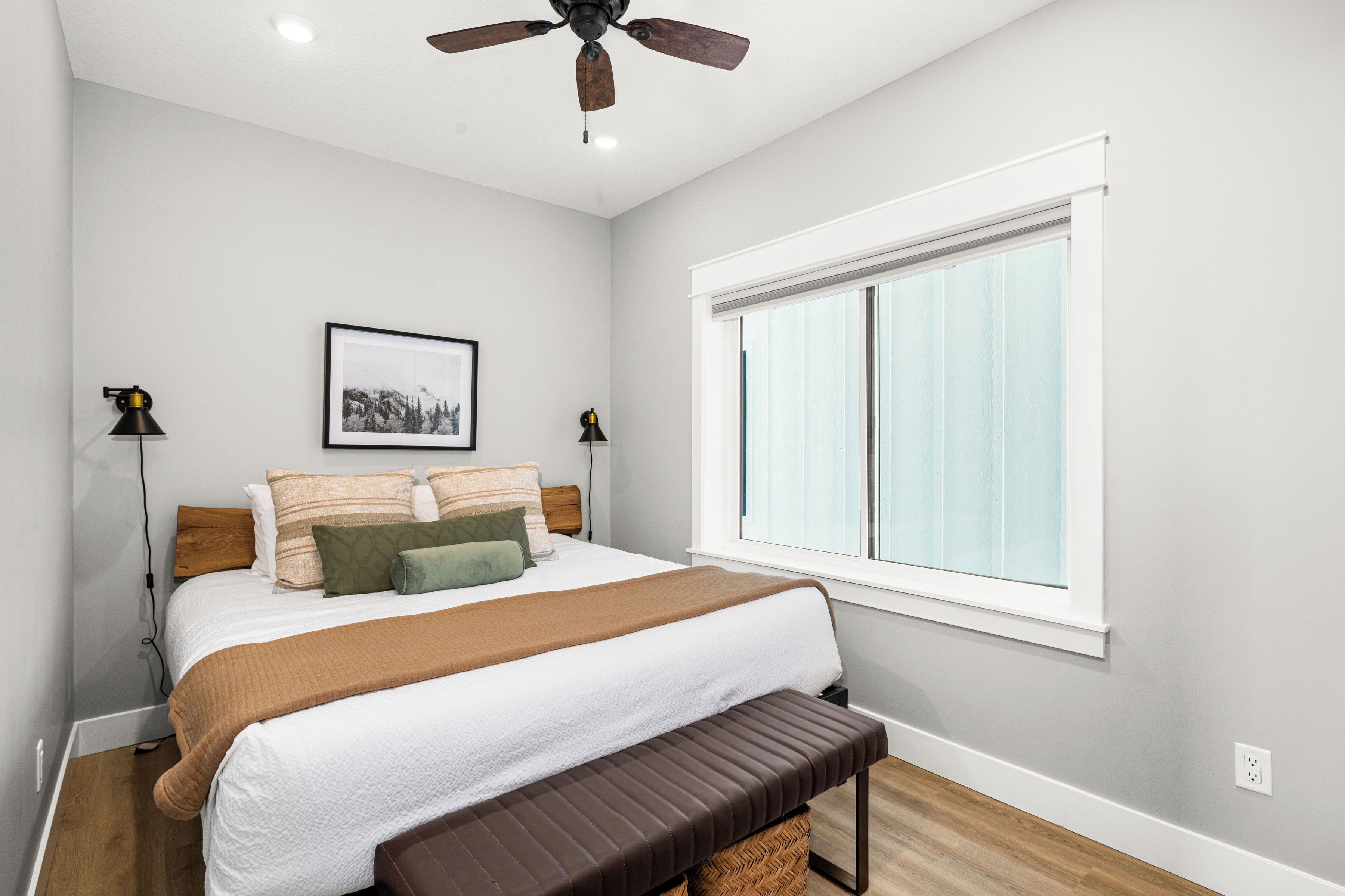 A bedroom with a bed, a ceiling fan, a window, and a bedside table.