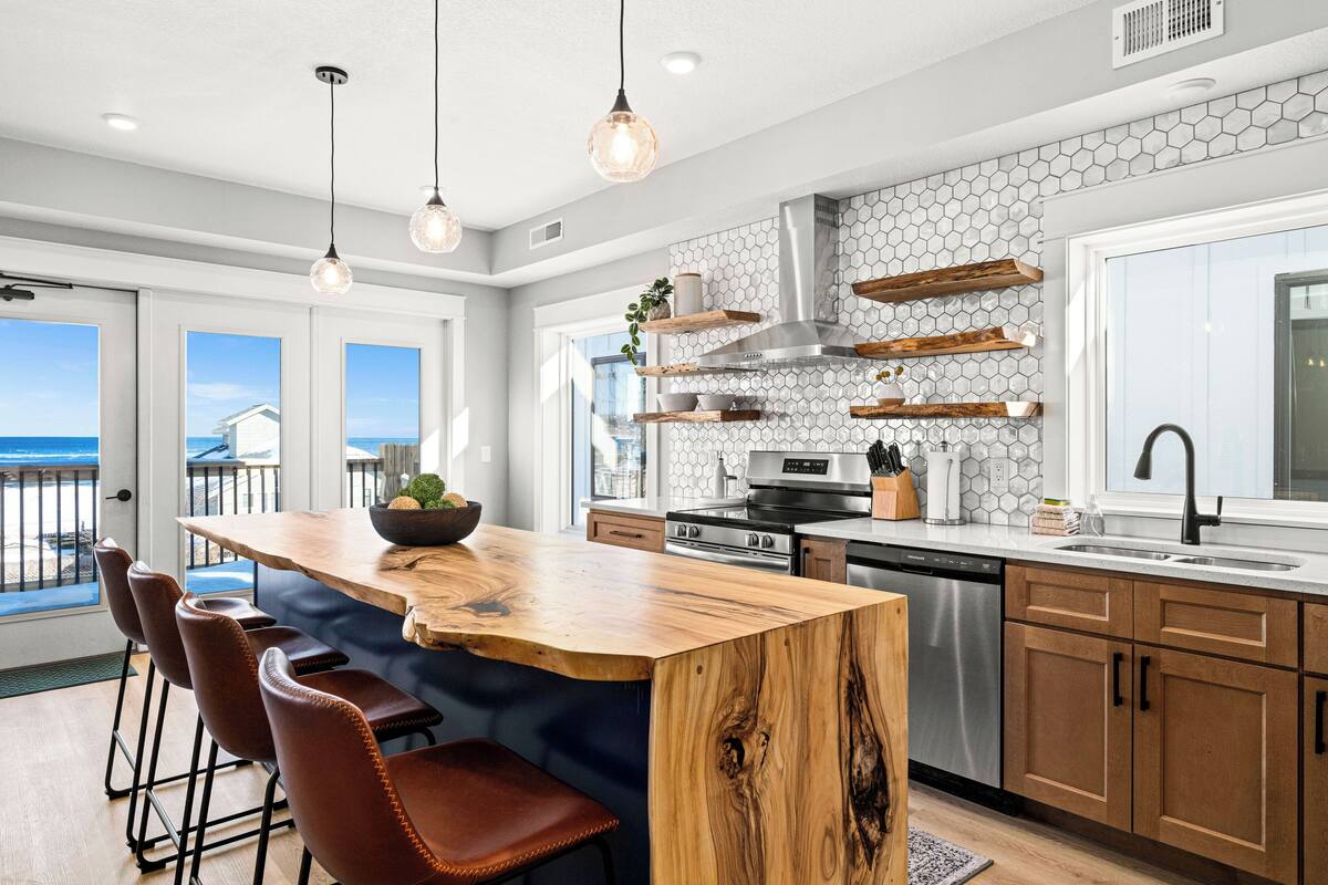A modern kitchen with a large island, bar stools, and a view of the ocean.
