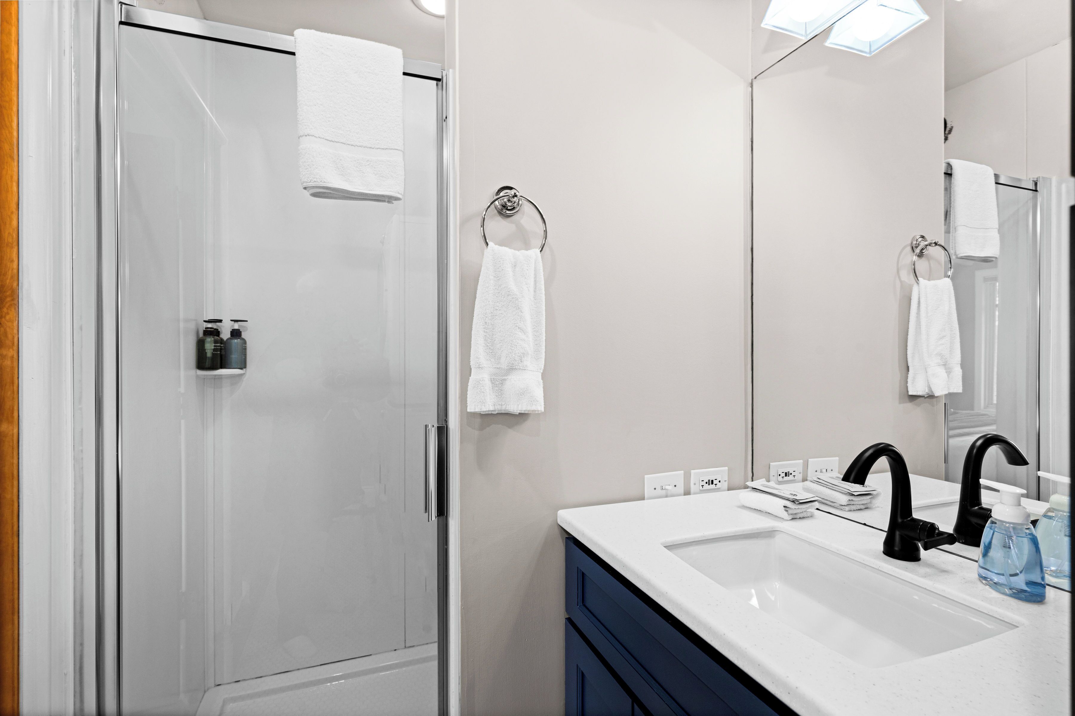 A modern bathroom with a glass shower enclosure, a white sink with a black faucet, and a mirror reflecting the room.