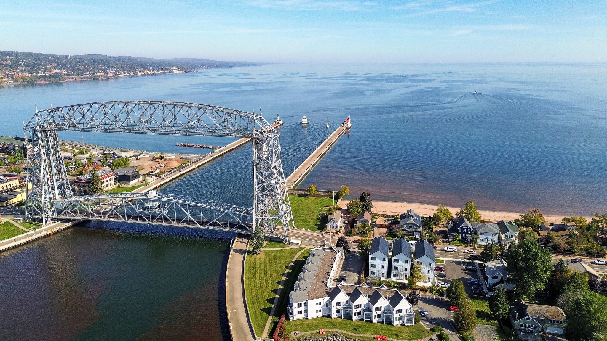 A large steel bridge spanning a river with residential buildings and a beach nearby.