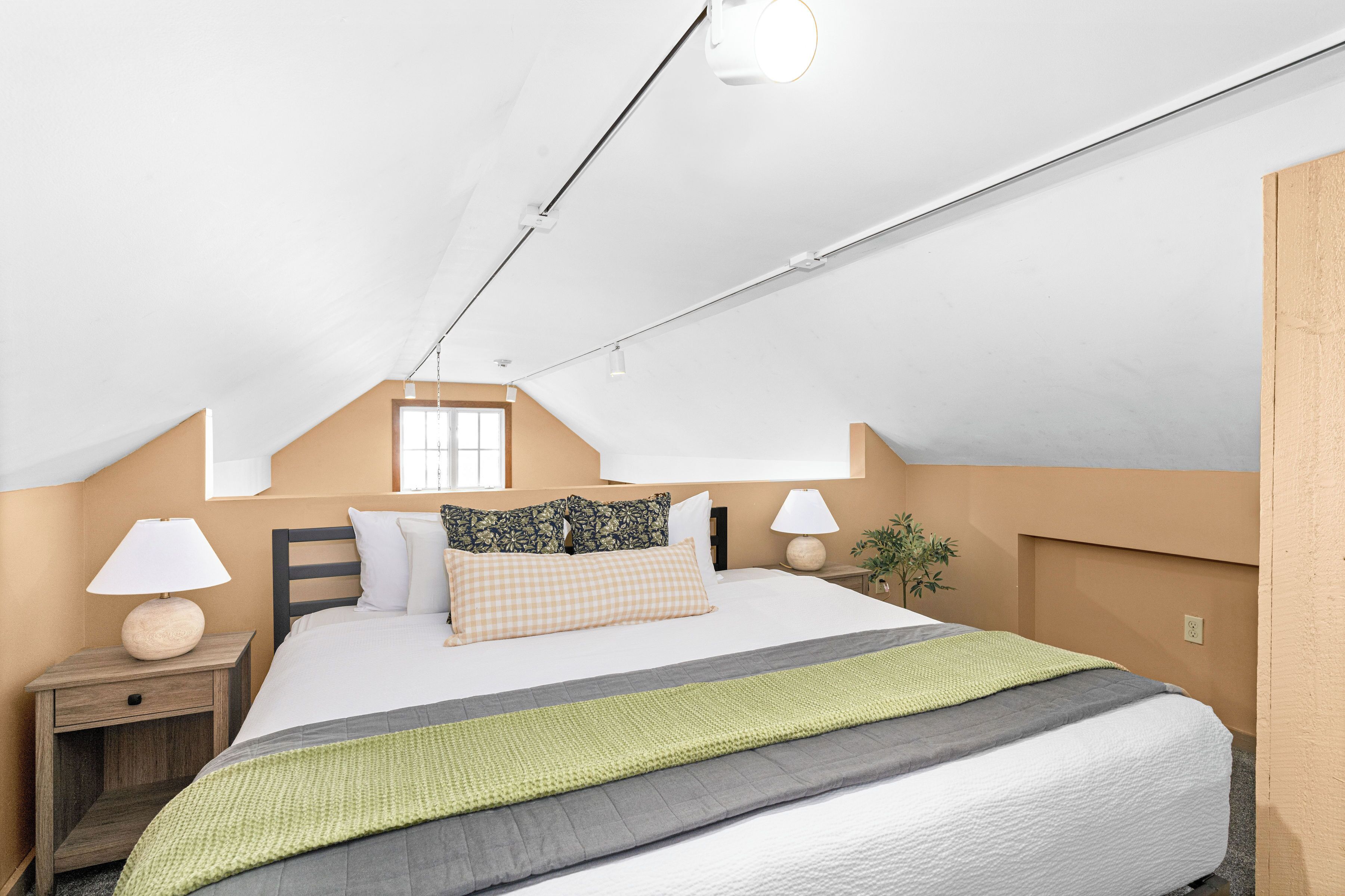 Una camera da letto con un letto, comodini, lampade, una finestra e una pianta.