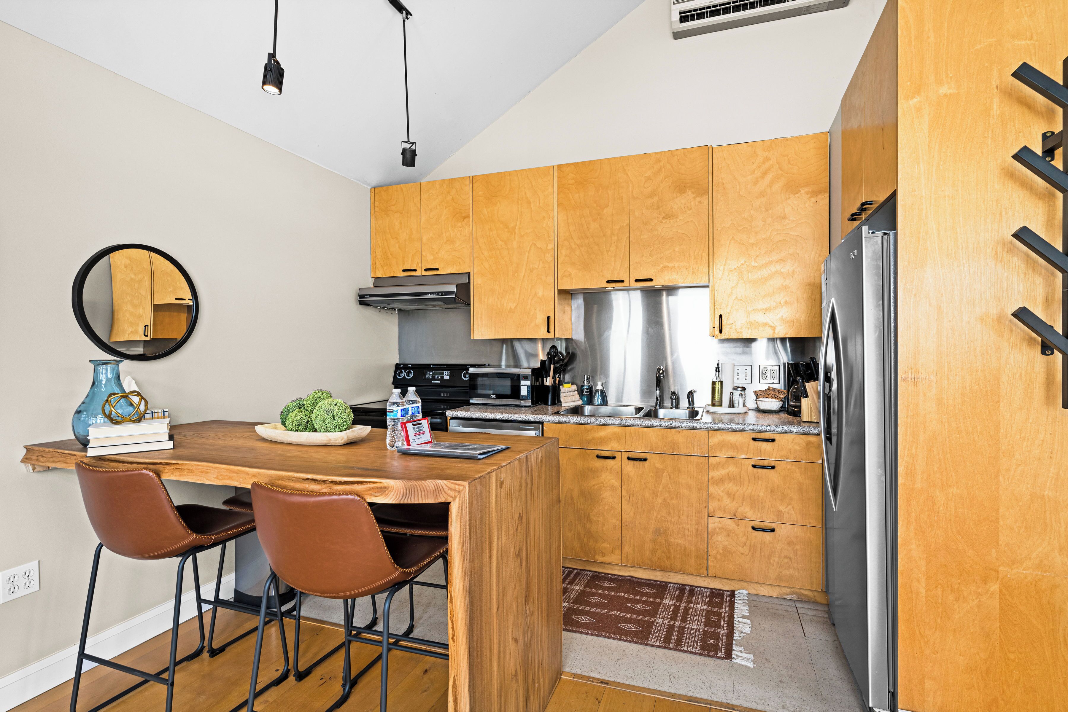 A modern kitchen with wooden cabinets, stainless steel appliances, and a dining area with a wooden table and chairs.