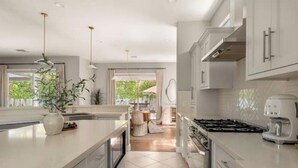 A modern kitchen with white cabinetry, a central island, a stove, and a coffee maker. - Desert Serenity: Pool, Sauna, Gym, Hot Tub, Bocce (Palm Springs)