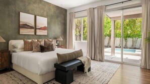 A bedroom with a large bed, a bench, a nightstand, and a view of a swimming pool. - Desert Serenity: Pool, Sauna, Gym, Hot Tub, Bocce (Palm Springs)