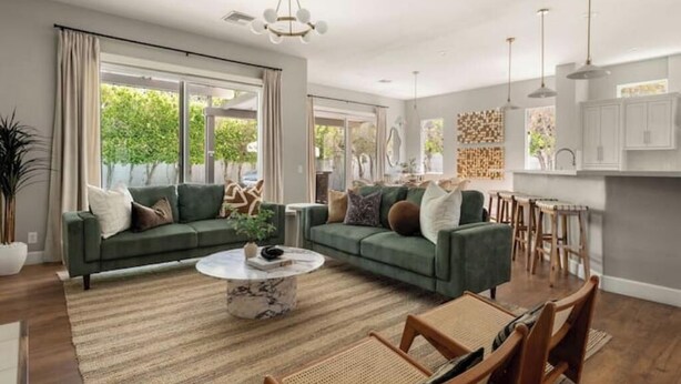 A spacious living room with a green sofa, a coffee table, and a dining area with wooden chairs. - Desert Serenity: Pool, Sauna, Gym, Hot Tub, Bocce (Palm Springs)