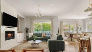 A modern living room with a fireplace, green sofas, a coffee table, and a dining area with chairs. - Desert Serenity: Pool, Sauna, Gym, Hot Tub, Bocce (Palm Springs)