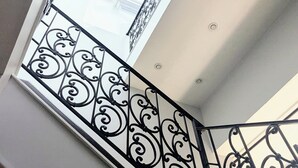 Eine Treppe mit aufwendiger schwarzer Geländerkonstruktion und einem großen Fenster mit geometrischem Muster.