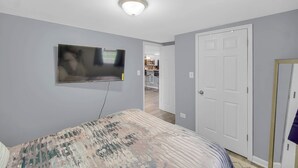 A bedroom with a bed, a flat-screen TV mounted on the wall, a door, and a hallway leading to a kitchen area. - Spacious 3 BDR/1 Bath - 1 mi from UChicago - Perfect for Traveling Professionals (Chicago)