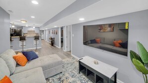 A modern living room with a grey sofa, a coffee table, and a large mirror reflecting a grey sofa and a painting. - Spacious 3 BDR/1 Bath - 1 mi from UChicago - Perfect for Traveling Professionals (Chicago)