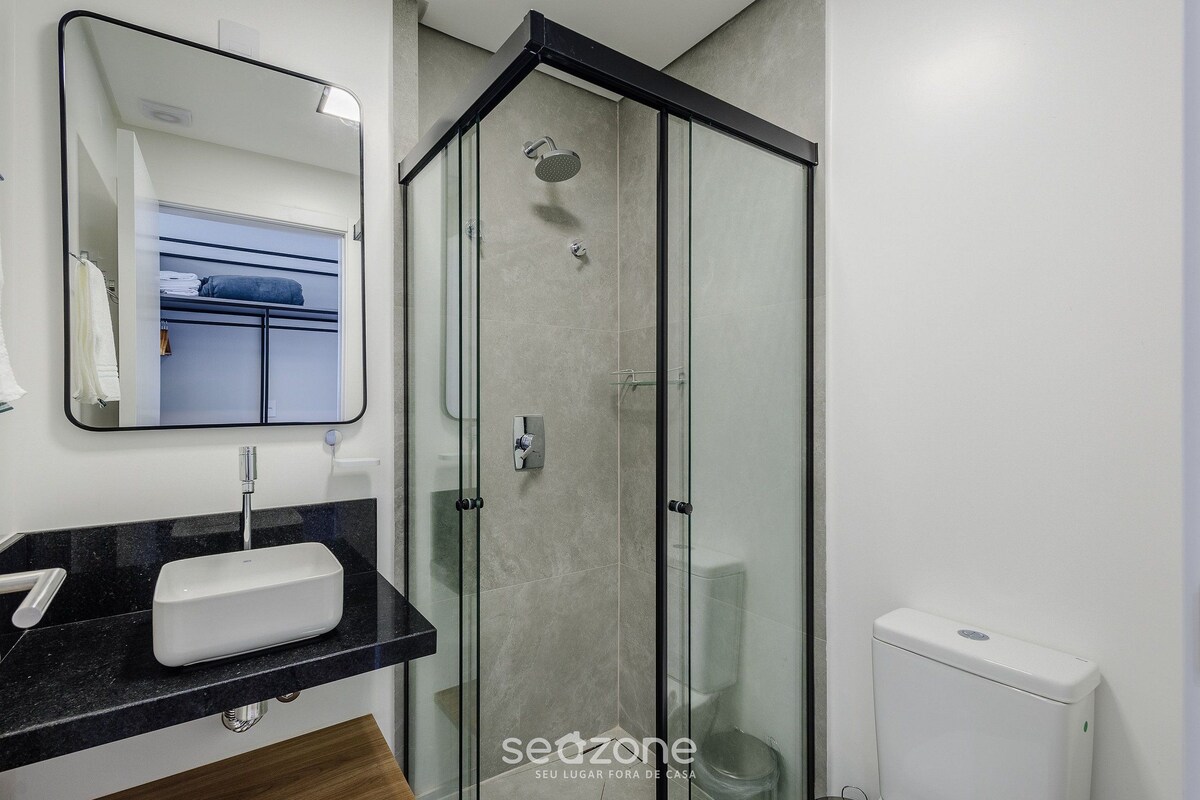 Un baño moderno con ducha envuelta en vidrio, lavamanos con encimera negra y un inodoro.
