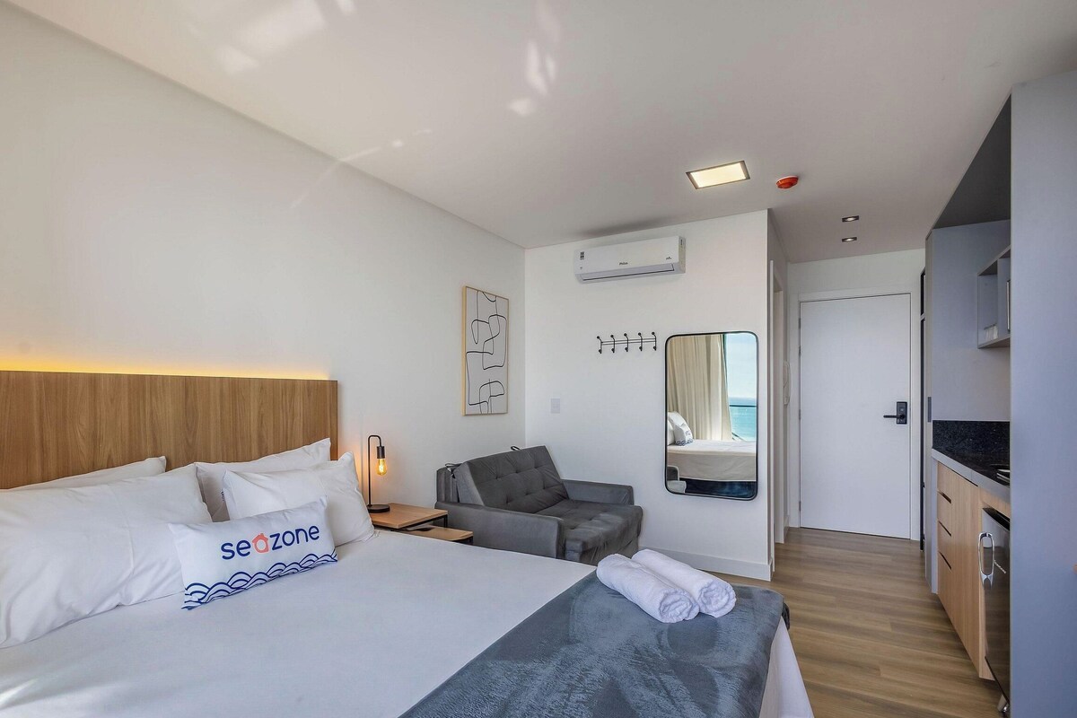 Una habitación de hotel con una cama, un escritorio, una silla, un espejo y una kitchenette.