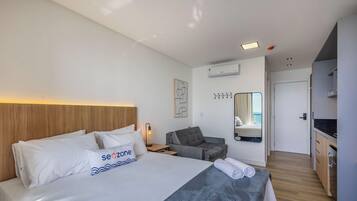 A hotel room with a bed, bedside table, lamp, chair, and a view of the sea through a window.