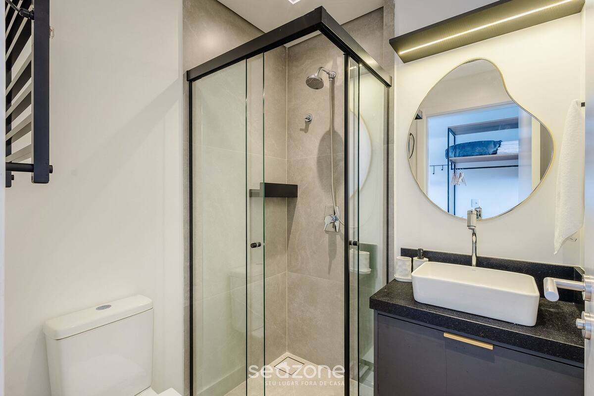 A modern bathroom with a glass-enclosed shower, a white sink, and a round mirror.