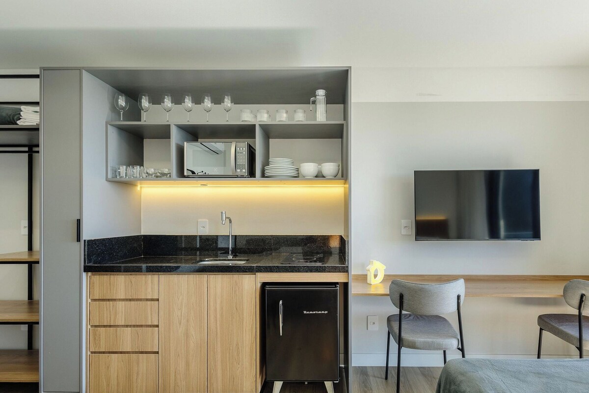A compact kitchen with a built-in refrigerator, a microwave, and a sink. There is a dining area with two chairs and a table, and a flat-screen TV mounted on the wall.