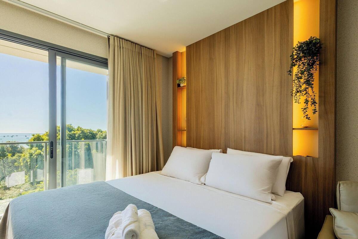 A hotel room with a large bed, a view of the sea, and a wooden accent wall.