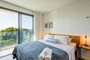 A modern hotel room with a large bed, a nightstand, a lamp, and a view of greenery through large windows. - Studios With Sea View at Penha Spot PSO - VF (Penha)