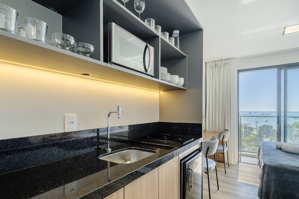 A modern kitchen with a black countertop, stainless steel sink, and a dining area with chairs and a table.