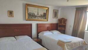 Camera d'albergo con due letti singoli, una testiera in legno, un piccolo mobiletto in legno e una fotografia incorniciata della Torre Eiffel.