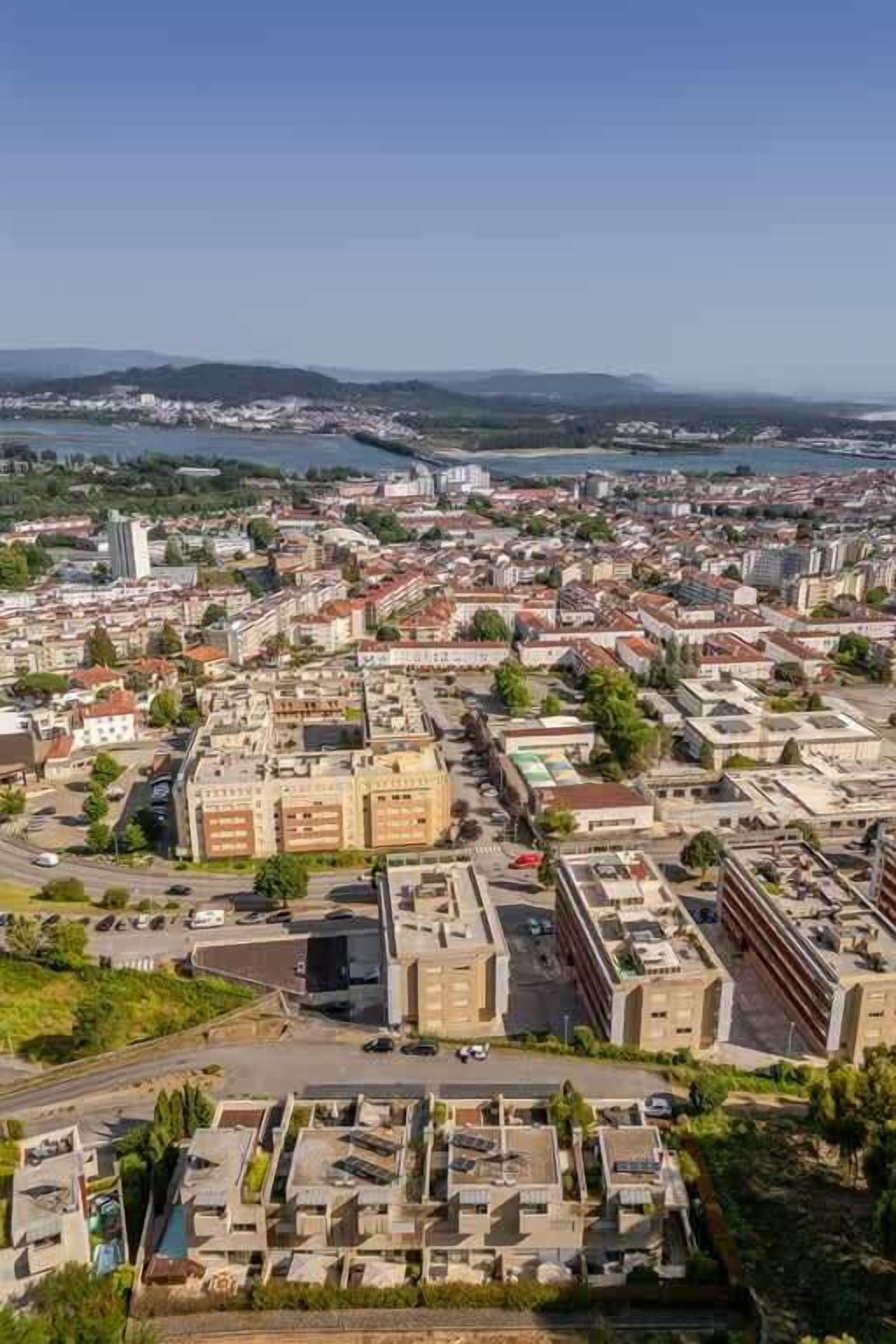 Ein Luftbild einer Stadtlandschaft mit einer Mischung aus Wohn- und Geschäftsgebäuden, einem Fluss im Hintergrund und blauem Himmel.